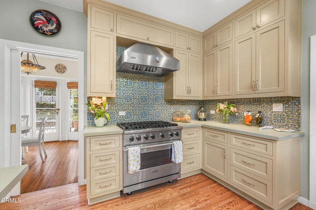 kitchen featuring tasteful backsplash, wall chimney exhaust hood, high end stainless steel range, and cream cabinetry