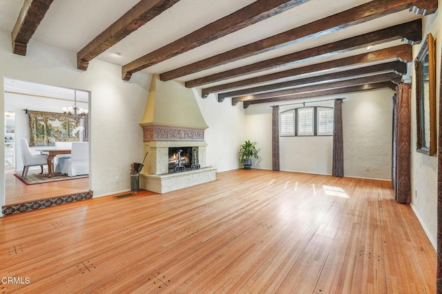 unfurnished living room featuring beam ceiling, an inviting chandelier, a fireplace, and light hardwood / wood-style flooring