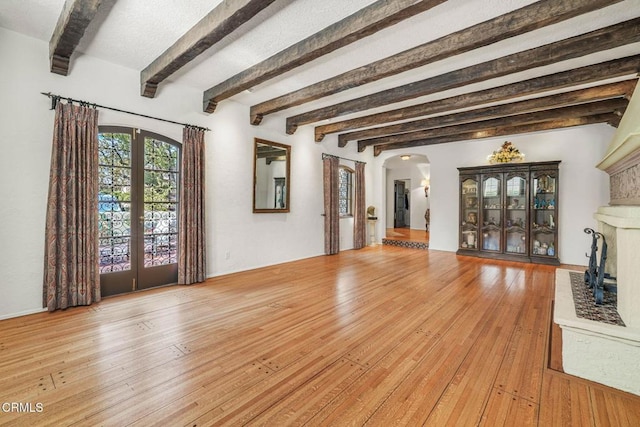 unfurnished living room featuring beam ceiling, light hardwood / wood-style floors, and french doors