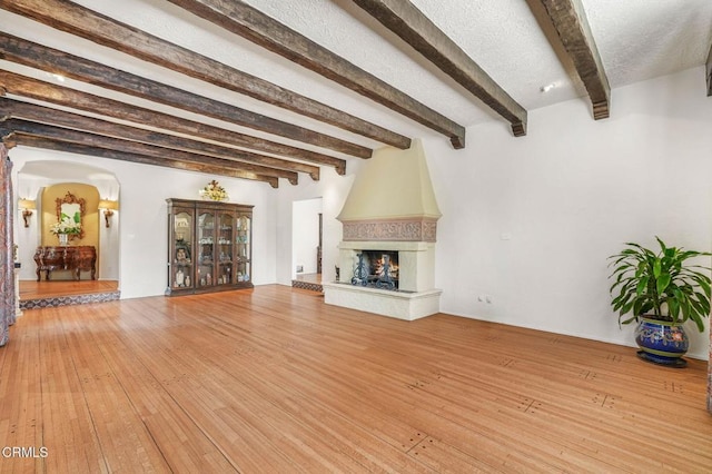 unfurnished living room with beamed ceiling, wood-type flooring, a textured ceiling, and a fireplace