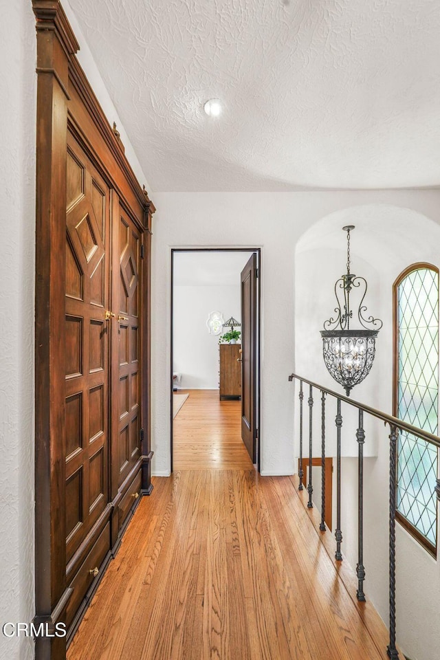 hallway featuring a notable chandelier, a textured ceiling, and light hardwood / wood-style flooring