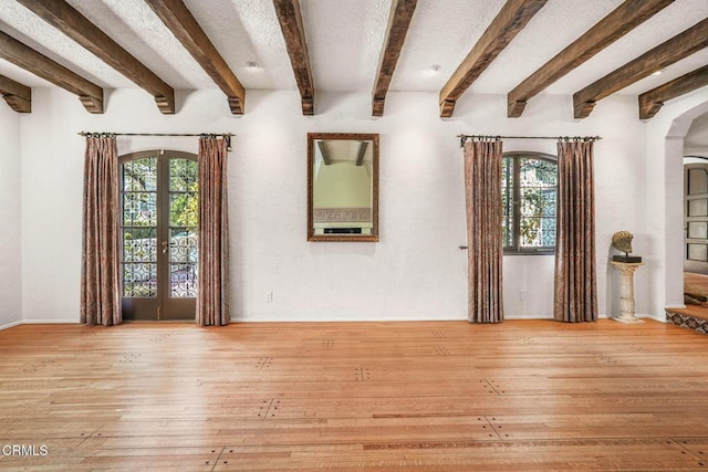 interior space with a healthy amount of sunlight, light hardwood / wood-style flooring, beam ceiling, and french doors