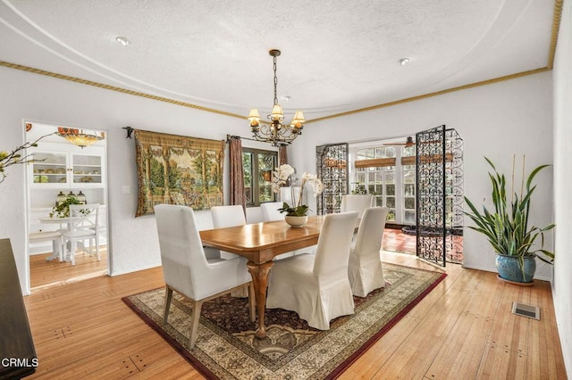 dining area with crown molding, an inviting chandelier, a textured ceiling, and light hardwood / wood-style floors