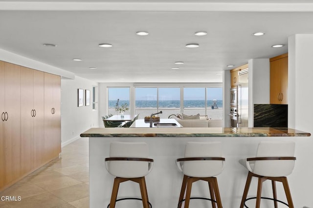 kitchen with a water view, a kitchen bar, kitchen peninsula, and sink