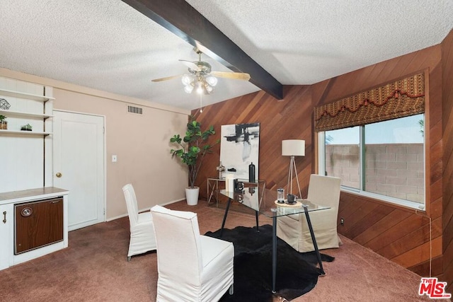 dining area with wood walls, dark colored carpet, a textured ceiling, ceiling fan, and beam ceiling