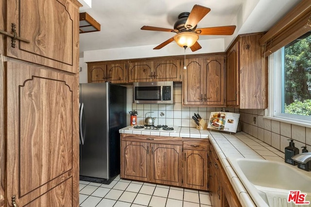 kitchen with sink, tasteful backsplash, tile countertops, light tile patterned floors, and stainless steel appliances