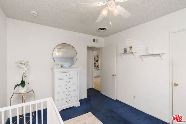 bedroom featuring ceiling fan, a textured ceiling, and dark colored carpet