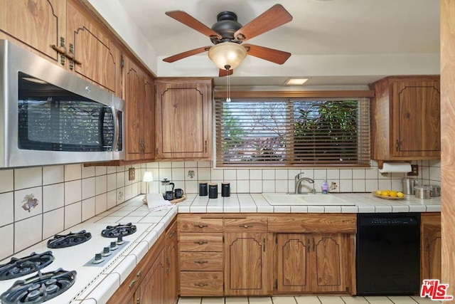 kitchen with white gas stovetop, tile countertops, sink, black dishwasher, and decorative backsplash