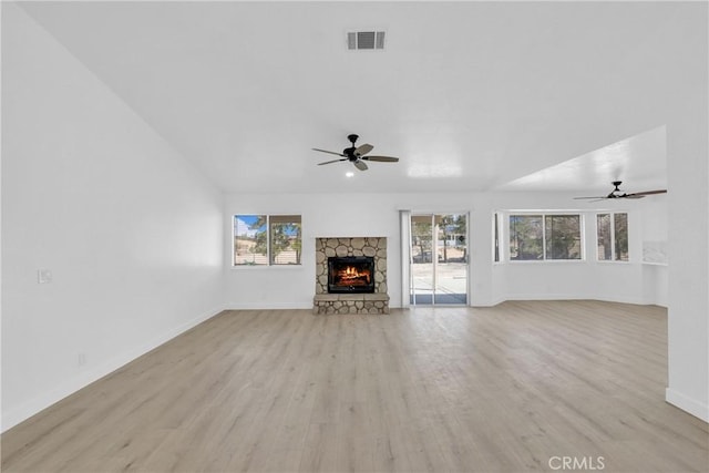 unfurnished living room with ceiling fan, a stone fireplace, and light hardwood / wood-style floors