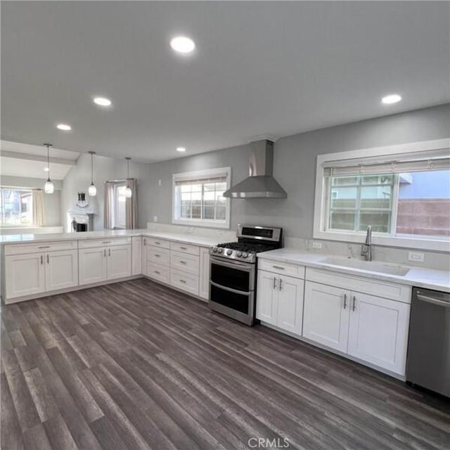 kitchen featuring wall chimney exhaust hood, sink, decorative light fixtures, stainless steel appliances, and white cabinets