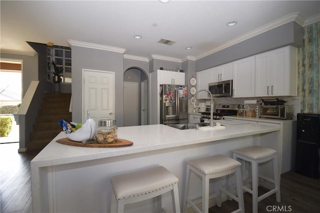 kitchen with stainless steel appliances, white cabinetry, ornamental molding, and a center island with sink