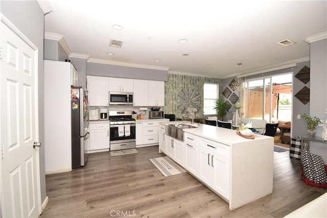 kitchen featuring sink, wood-type flooring, ornamental molding, stainless steel appliances, and white cabinets