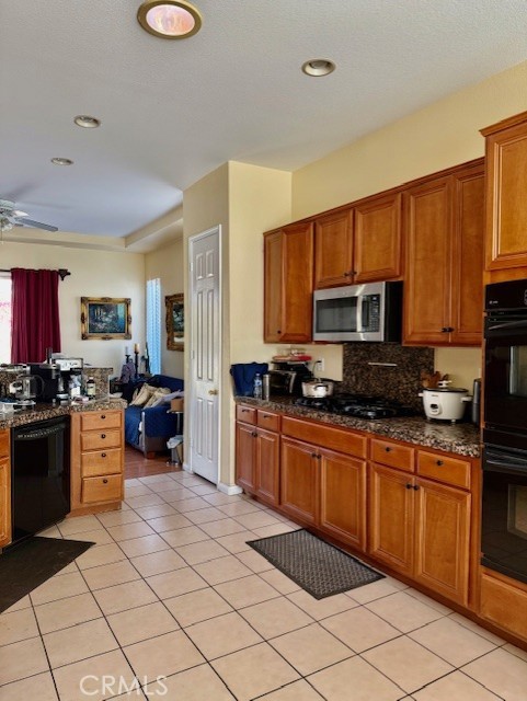 kitchen featuring light tile patterned flooring, tasteful backsplash, dark stone countertops, ceiling fan, and black appliances