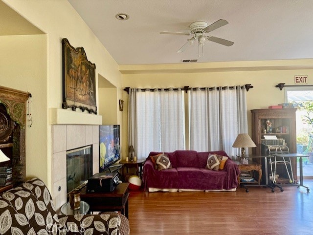 living room featuring wood-type flooring, a tile fireplace, and ceiling fan