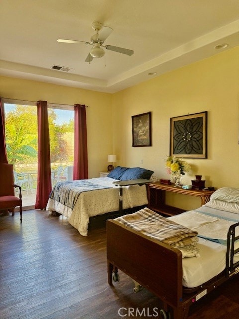 bedroom with dark hardwood / wood-style flooring, a tray ceiling, access to outside, and ceiling fan