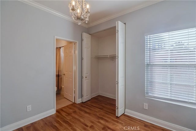 unfurnished bedroom featuring hardwood / wood-style flooring, crown molding, a closet, and a notable chandelier