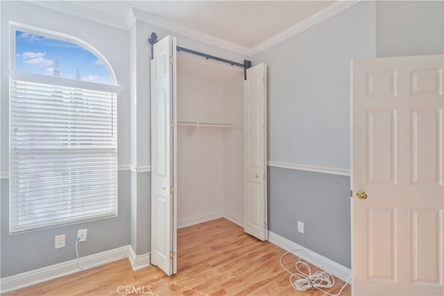 unfurnished bedroom with a closet, crown molding, a barn door, and light wood-type flooring