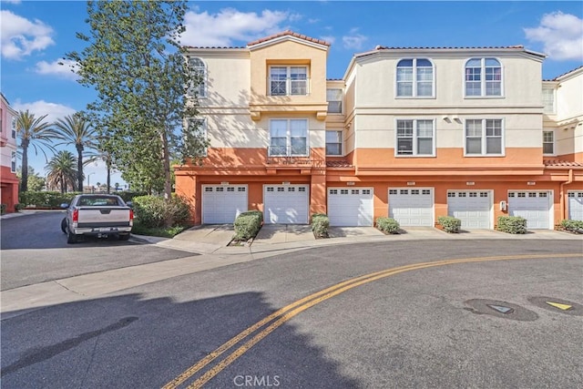 townhome / multi-family property with a garage, driveway, stucco siding, and a tile roof
