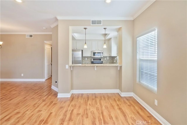 kitchen with appliances with stainless steel finishes, decorative light fixtures, white cabinets, decorative backsplash, and kitchen peninsula