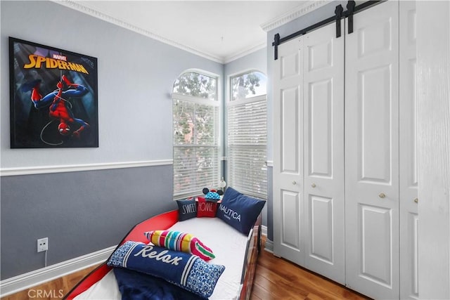 bedroom featuring a barn door, a closet, crown molding, and wood finished floors