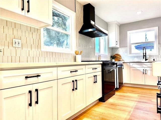 kitchen featuring sink, black electric range oven, decorative backsplash, wall chimney range hood, and light wood-type flooring