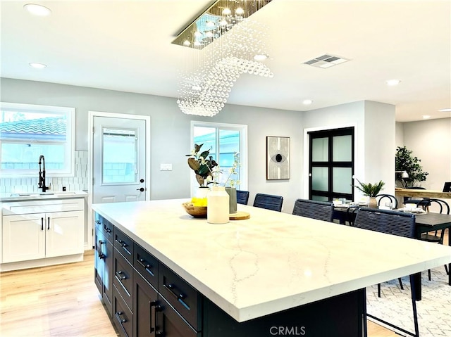 kitchen with sink, light hardwood / wood-style flooring, a kitchen island, light stone countertops, and white cabinets