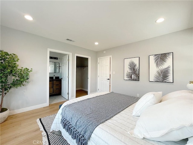 bedroom featuring ensuite bath, a spacious closet, and light wood-type flooring