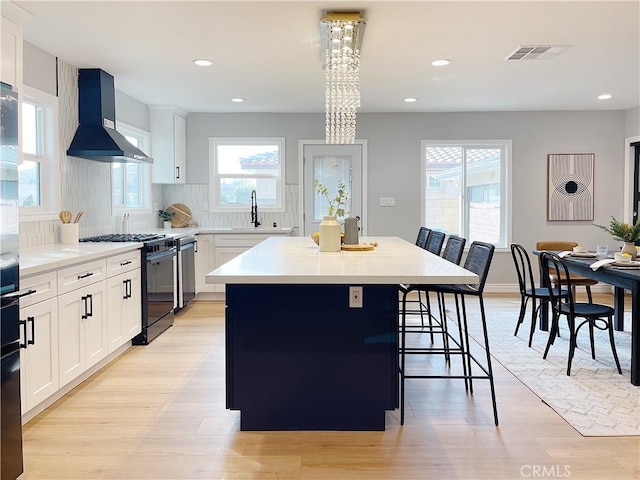 kitchen with a kitchen bar, a center island, wall chimney range hood, black gas range, and white cabinets