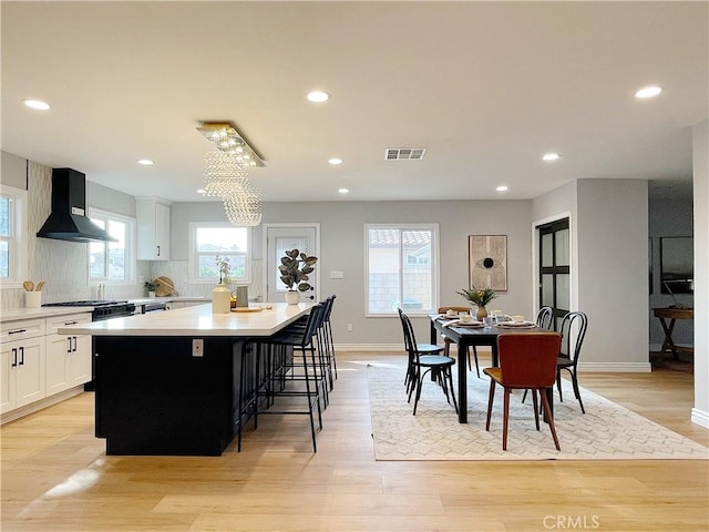 kitchen featuring a breakfast bar, white cabinetry, a kitchen island, wall chimney exhaust hood, and light wood-type flooring