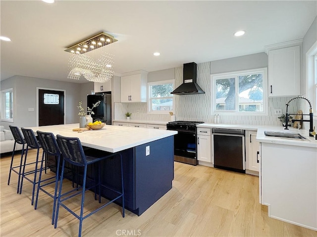 kitchen with sink, white cabinetry, a center island, wall chimney range hood, and black appliances