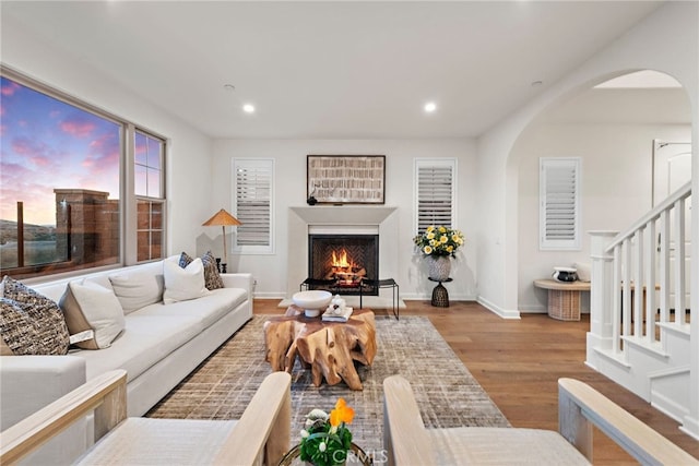 living area featuring a warm lit fireplace, light wood-style flooring, stairs, and recessed lighting