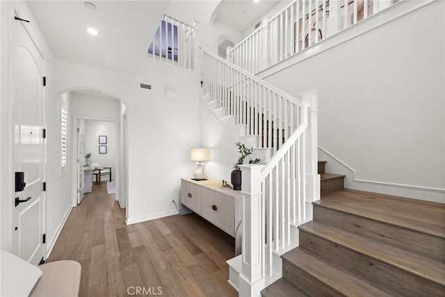 staircase featuring arched walkways, recessed lighting, a high ceiling, wood finished floors, and baseboards