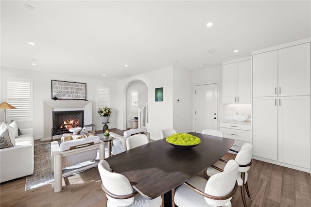 dining space featuring a warm lit fireplace, stairway, dark wood finished floors, and recessed lighting