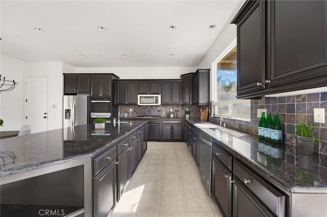 kitchen with appliances with stainless steel finishes, sink, dark stone countertops, backsplash, and light tile patterned floors