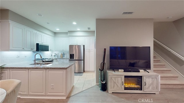 kitchen featuring appliances with stainless steel finishes, white cabinetry, backsplash, kitchen peninsula, and light stone countertops