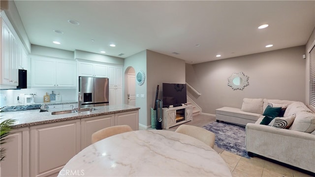 kitchen featuring sink, light tile patterned floors, white cabinetry, stainless steel refrigerator with ice dispenser, and light stone countertops