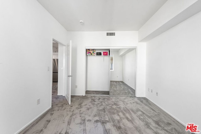 unfurnished bedroom with carpet flooring, stainless steel fridge, and a closet