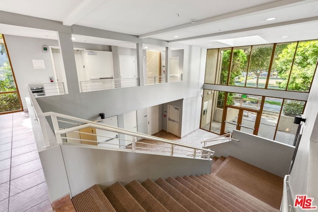 stairs with beam ceiling, tile patterned floors, and expansive windows