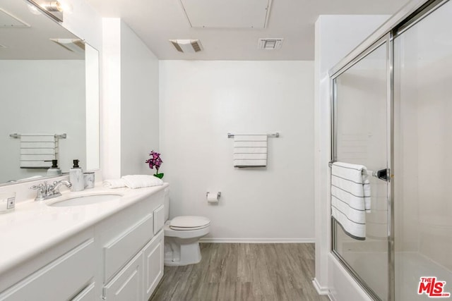 full bathroom featuring hardwood / wood-style flooring, enclosed tub / shower combo, vanity, and toilet