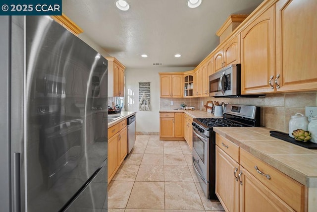 kitchen with tasteful backsplash, light brown cabinets, light tile patterned floors, tile counters, and stainless steel appliances