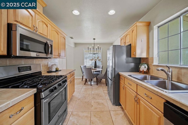 kitchen with pendant lighting, sink, appliances with stainless steel finishes, tasteful backsplash, and a chandelier