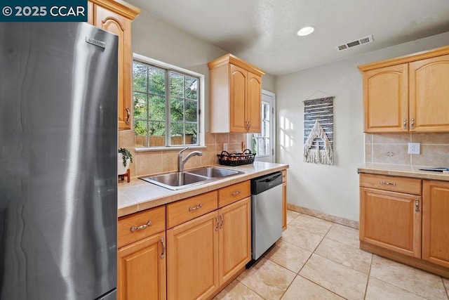 kitchen featuring sink, light tile patterned floors, appliances with stainless steel finishes, tile counters, and backsplash