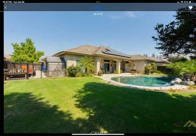 back of property featuring a yard, a fenced in pool, and solar panels