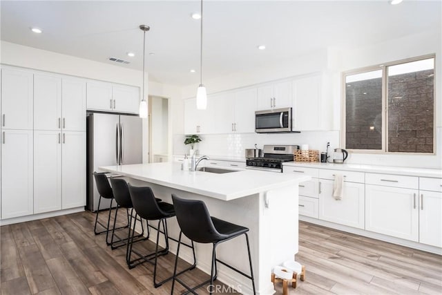 kitchen with sink, white cabinetry, decorative light fixtures, appliances with stainless steel finishes, and a kitchen island with sink