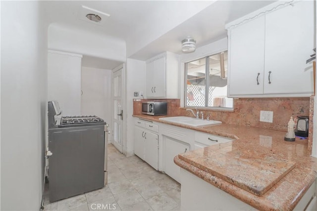 kitchen with tasteful backsplash, sink, white cabinets, light tile patterned floors, and gas range oven