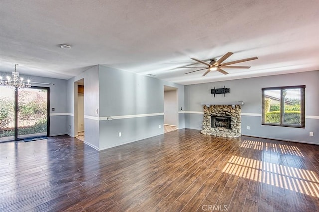 unfurnished living room featuring dark hardwood / wood-style floors, a stone fireplace, and ceiling fan with notable chandelier