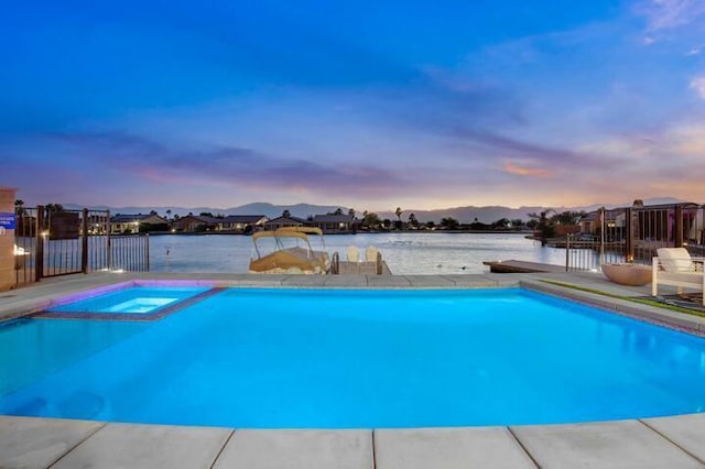 pool at dusk featuring an in ground hot tub and a water view