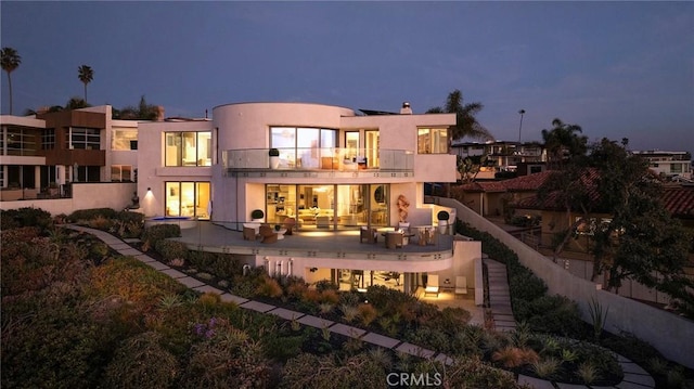 back house at dusk featuring a balcony, outdoor lounge area, and a patio