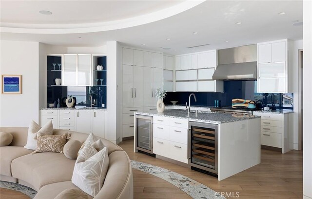 kitchen featuring white cabinets, a kitchen island with sink, beverage cooler, and wall chimney exhaust hood