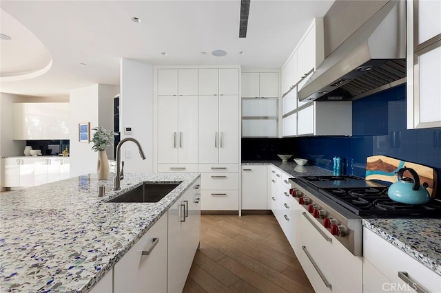 kitchen featuring sink, white cabinetry, stainless steel gas stovetop, light stone countertops, and wall chimney range hood